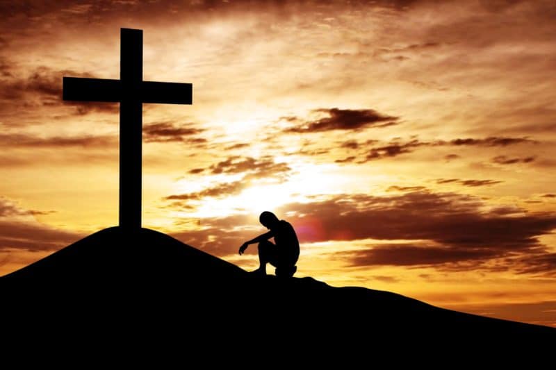 Silhouette of a man kneeling in front of a cross concept image for Christian rehab marketing