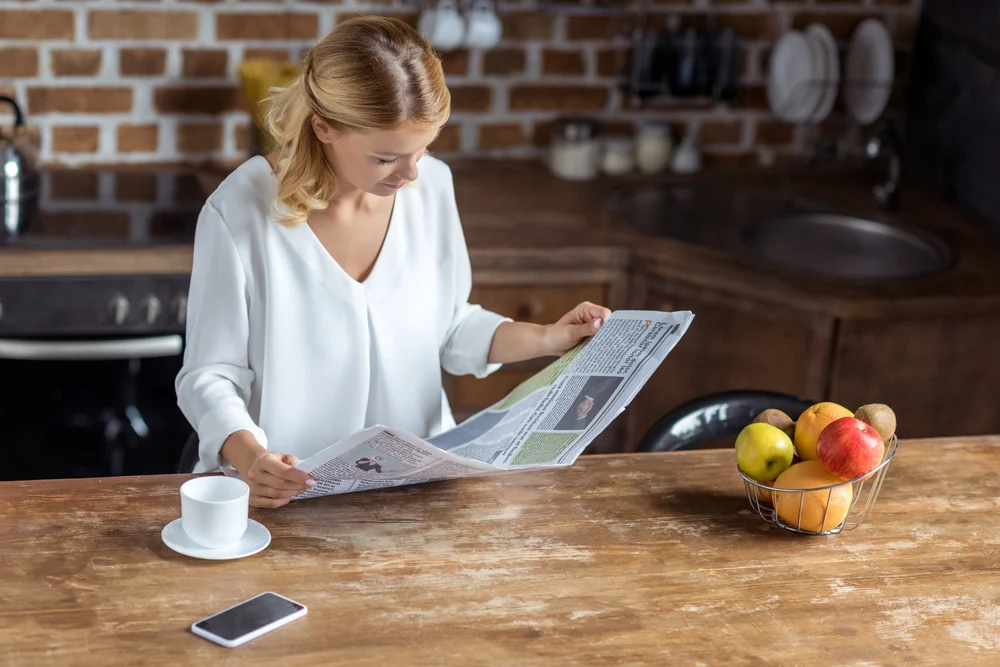 Depositphotos_166737606_S woman reading newspaper ads on kitchen counter