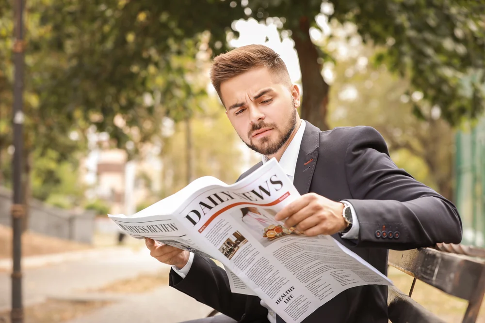 Depositphotos_320883006_S man in suit on a bench looking at newspaper advertisments