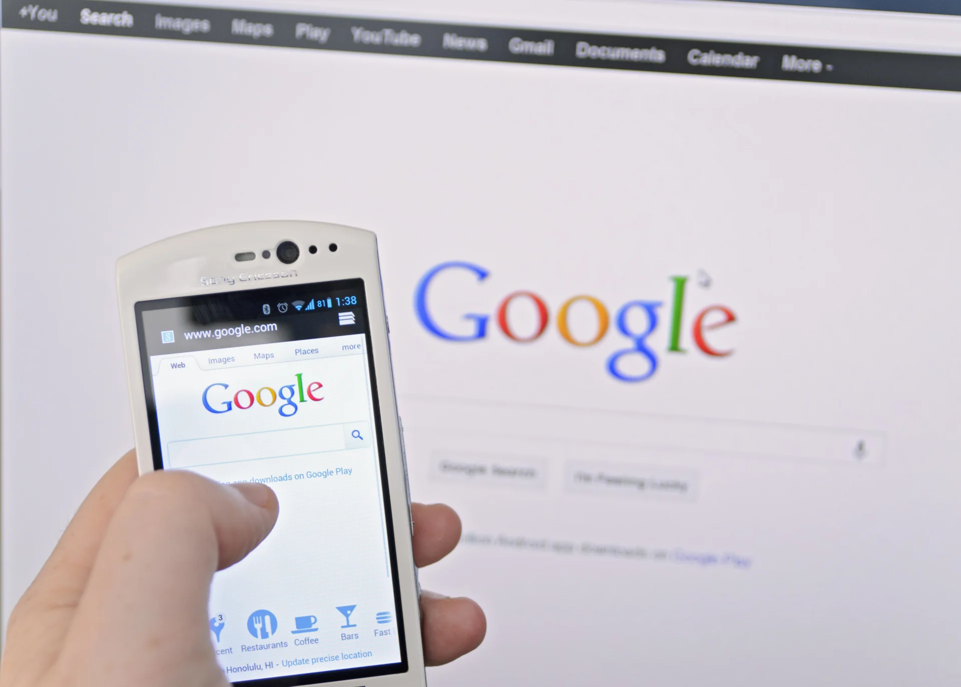 Google On Smartphone image of man on phone using google with desktop computer in the background
